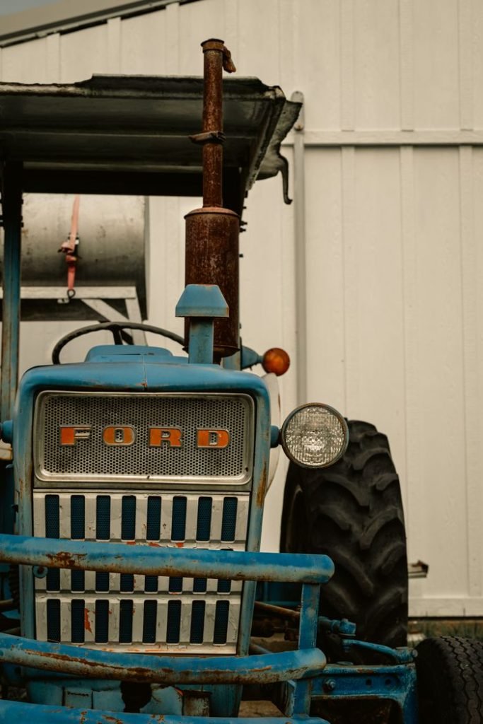 Close-up of an old Ford tractor parked by an outdoor garage.