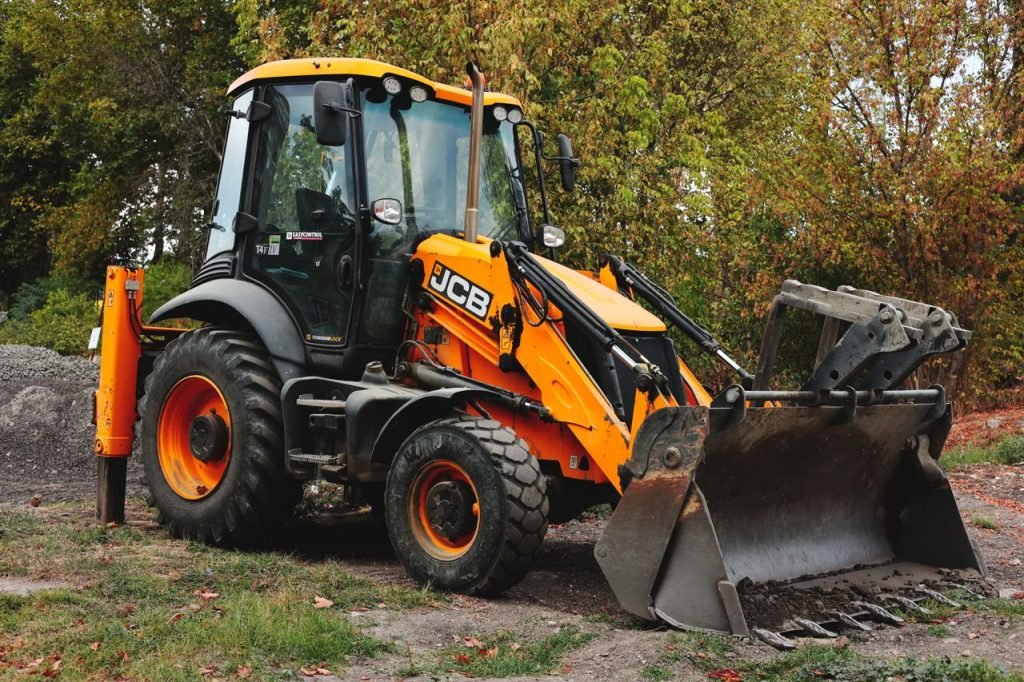 A bright yellow backhoe loader parked at a construction site surrounded by trees.